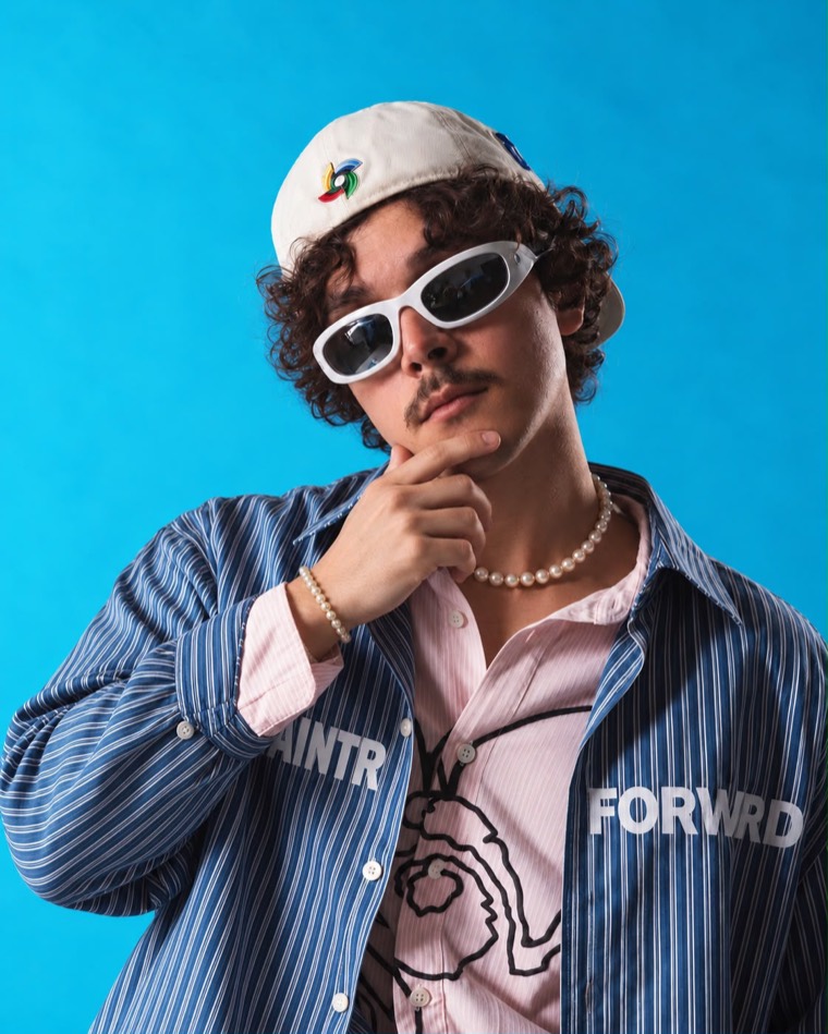 Deeko de boné, óculos brancos e colar de pérolas em fundo azul